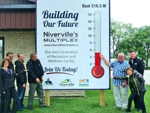 Heather Miller, Eric King, Clayton Smeltz, John Funk, Clarence Braun, Myron Dyck, and Libby Hanna raise the multiplex fundraising thermometer outside of the town office