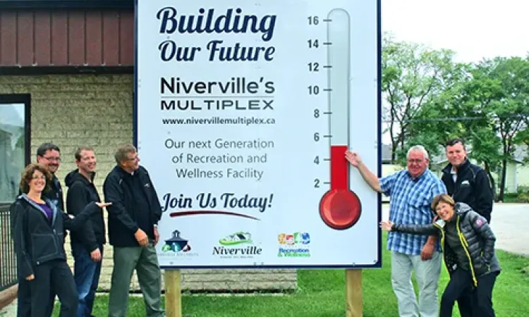 Heather Miller, Eric King, Clayton Smeltz, John Funk, Clarence Braun, Myron Dyck, and Libby Hanna raise the multiplex fundraising thermometer outside of the town office