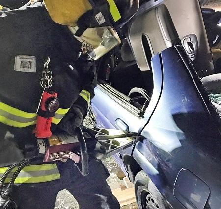 A Niverville firefighter using the jaws of life to open the dear door of a car.